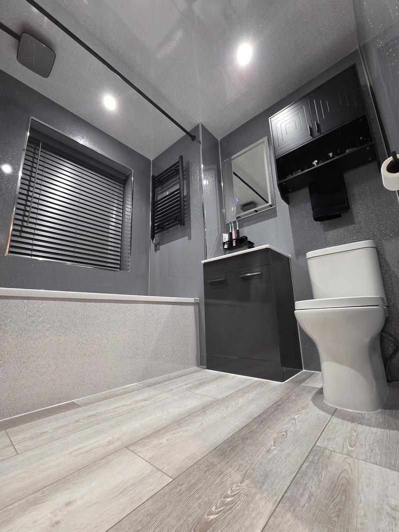 Bathroom seen from the corner with WC, vanity unit, black wall cabinet and bath
