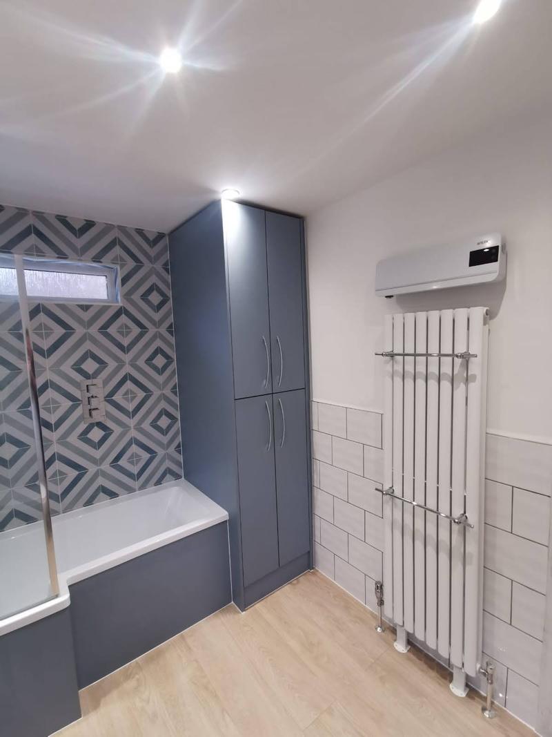 Bathroom with a bold geometric feature wall, a bath and a tall grey storage unit