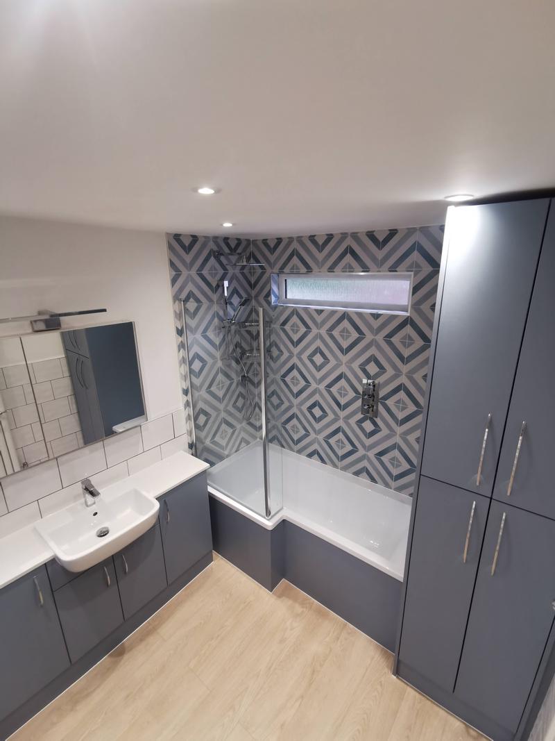 Bathroom with a geometric feature wall, grey fitted units and a bath with a glass screen