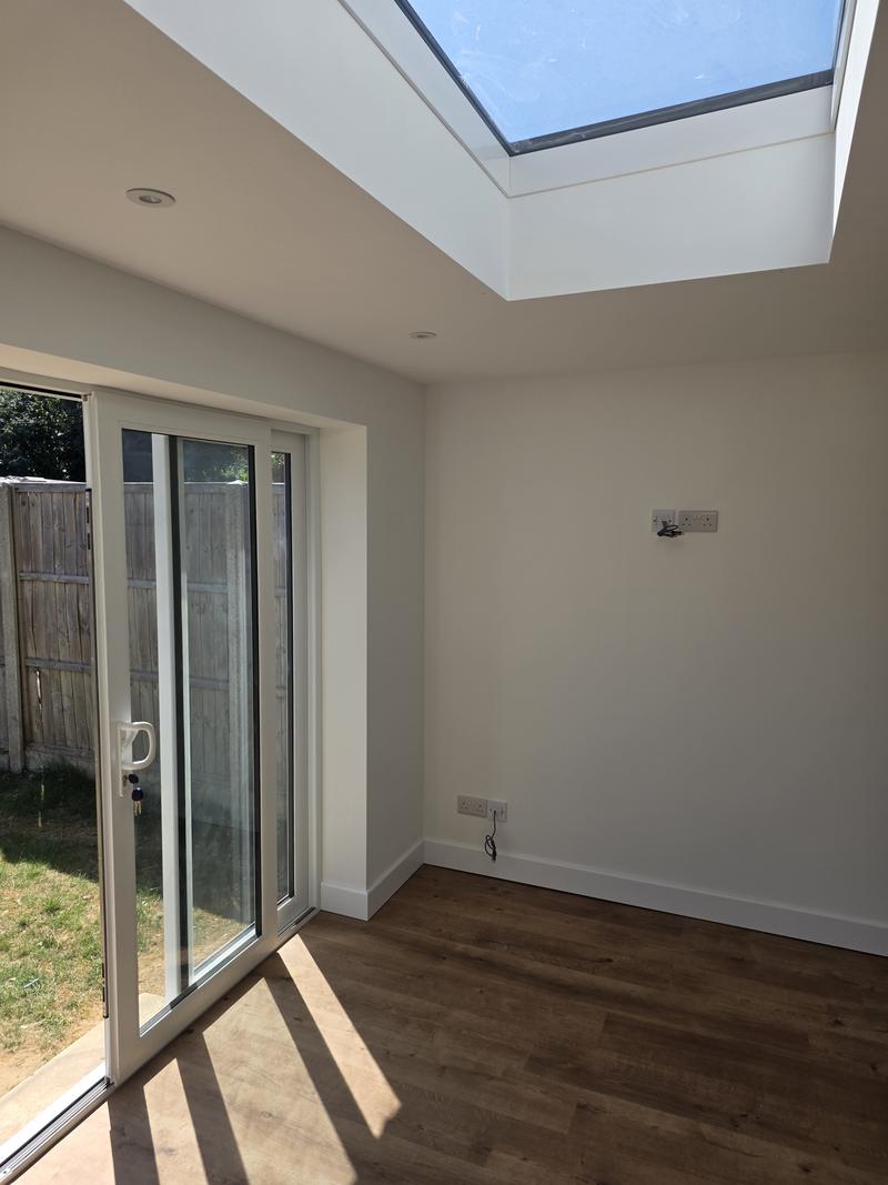 Completed extension from inside, with a large flush roof lantern and white sliding doors onto the garden