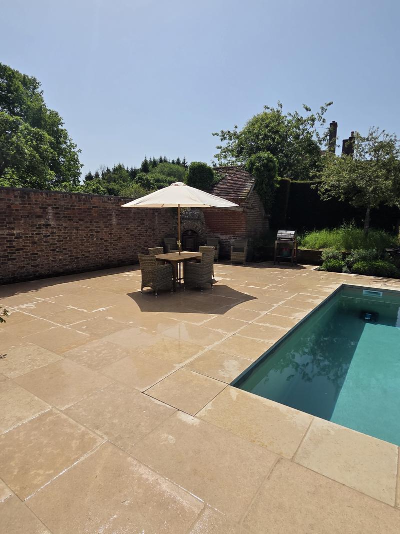Corner of the pool seen from the terrace, with a parasol and an old brick wall behind