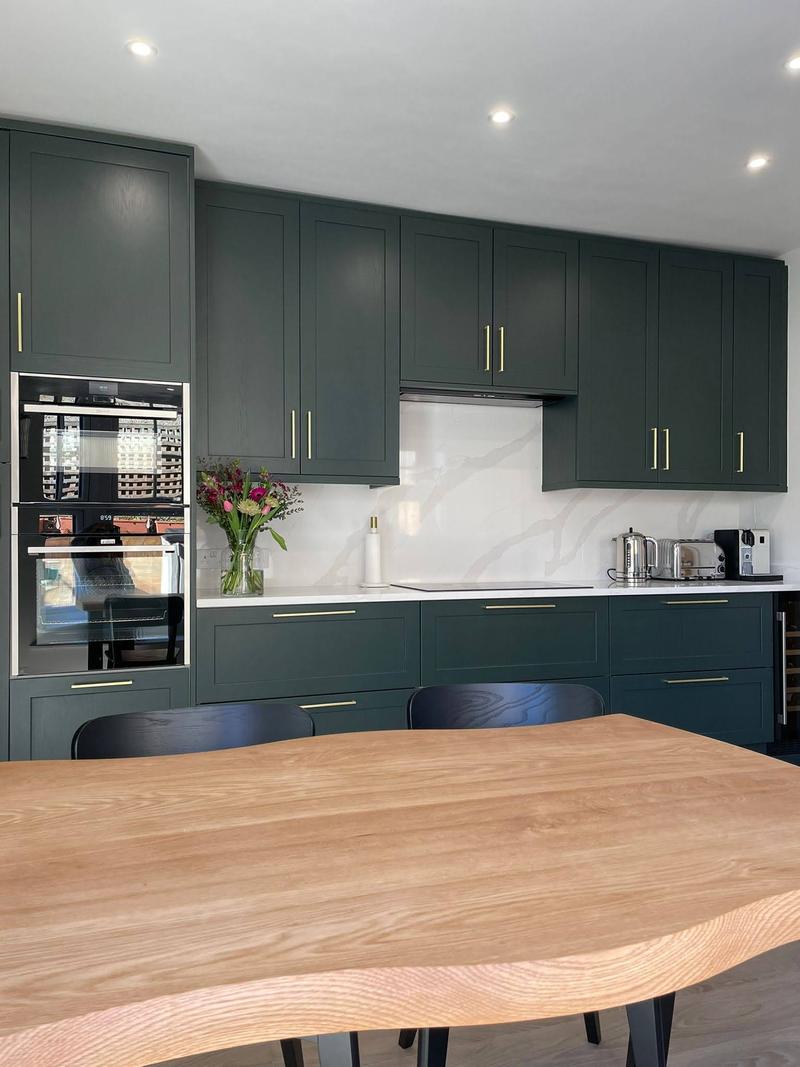 Dark green shaker kitchen with brass handles, quartz worktops and a live-edge oak table