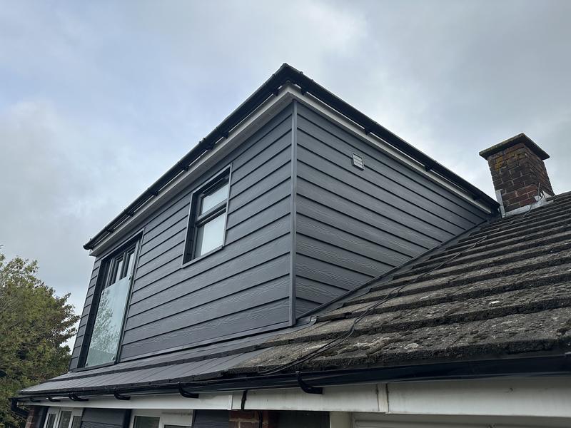 Finished dormer clad in dark grey boarding, set into a tiled roof beside a brick chimney