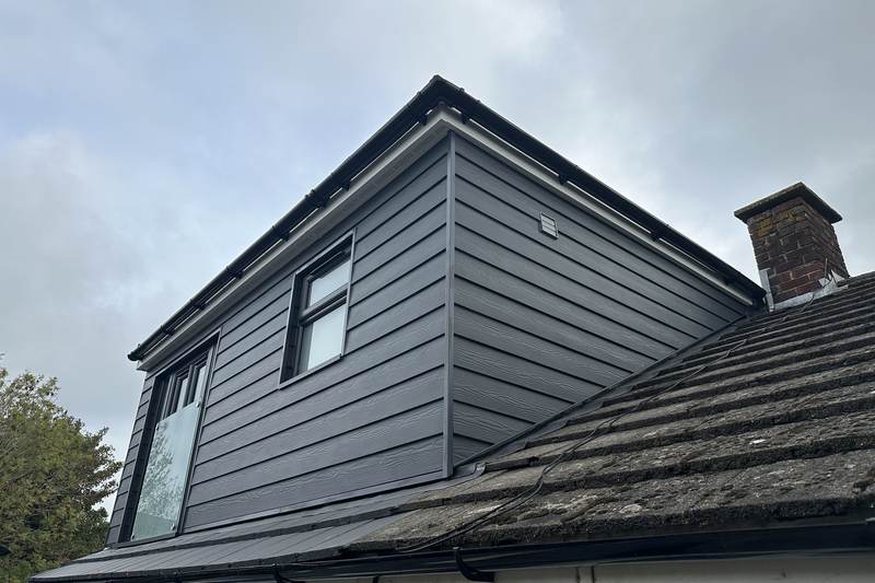 Finished dormer loft conversion clad in dark grey boarding, with a glazed gable end and a brick chimney beside it
