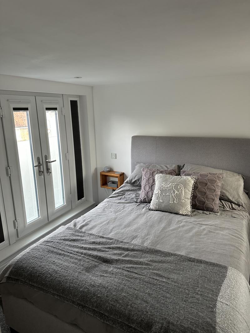 Finished loft bedroom with a double bed against a white wall and French doors to a balustrade