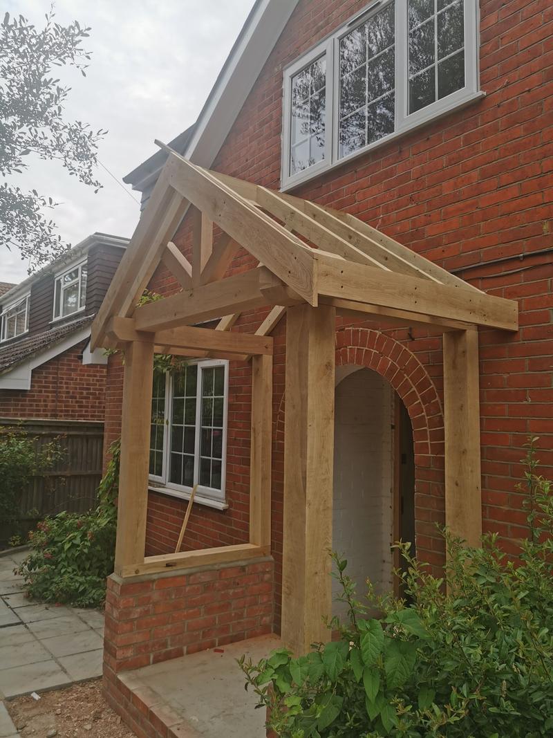 Green oak porch frame newly erected against a red-brick house