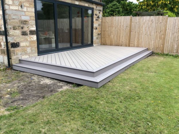 Grey composite decking with a bullnose step edge laid against a stone house with anthracite bifold doors