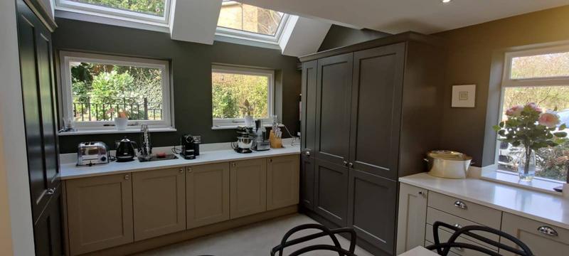 Kitchen run beneath two flush rooflights with tall larder cupboards and garden views