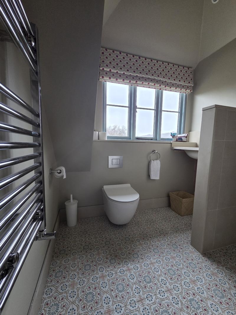 Loft bathroom under a sloping ceiling with a wall-hung WC and a patterned roman blind