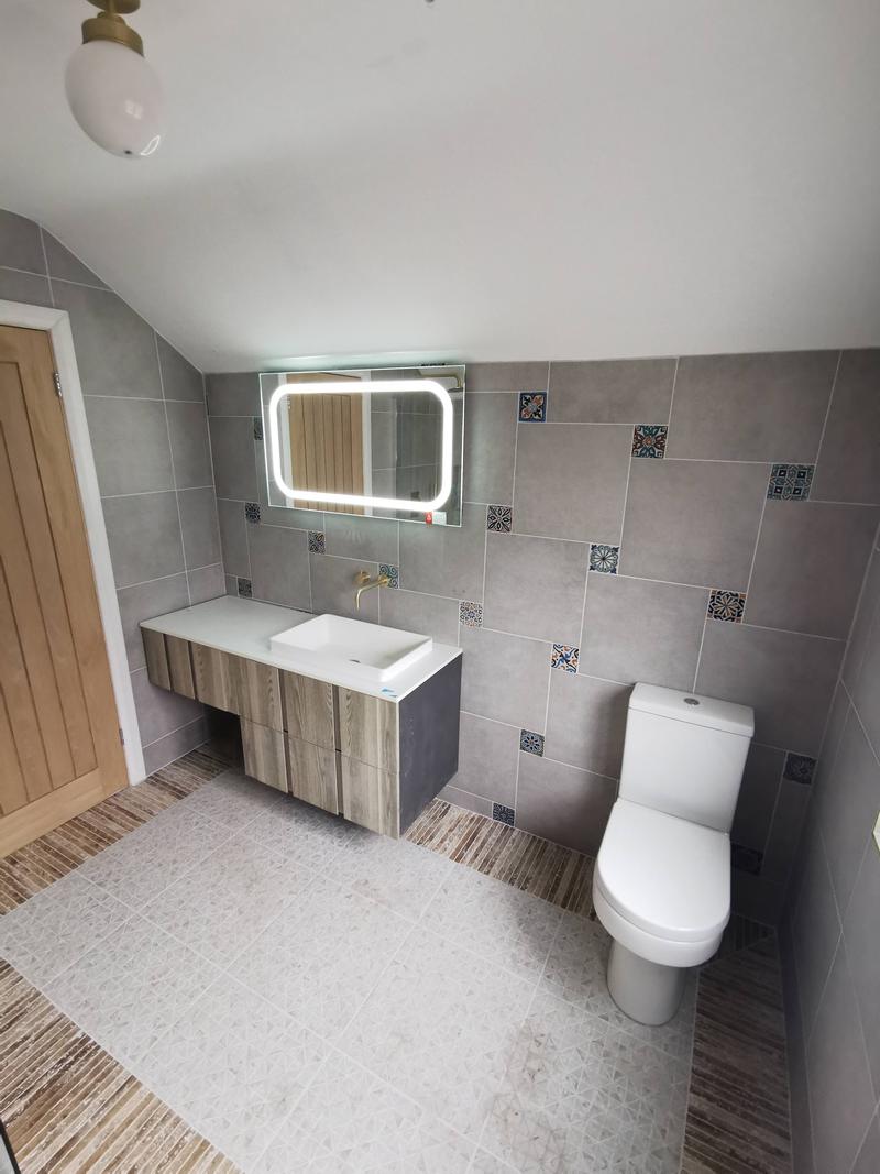 Loft shower room with patterned feature tiles, a wall-hung vanity and a lit mirror