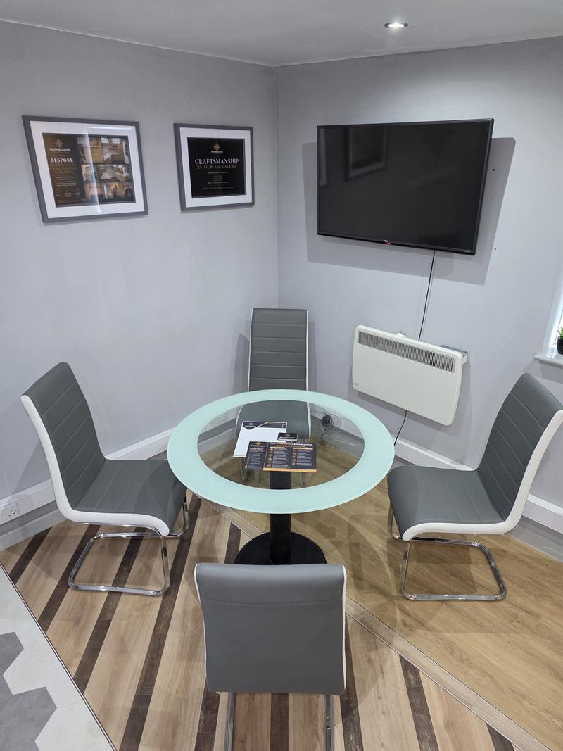 Meeting table with four chairs and a wall-mounted screen in the showroom