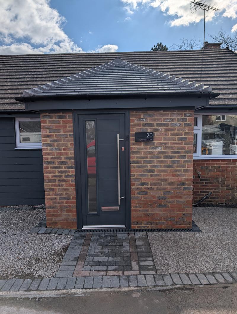 New brick entrance porch with a tiled hip roof and an anthracite composite front door