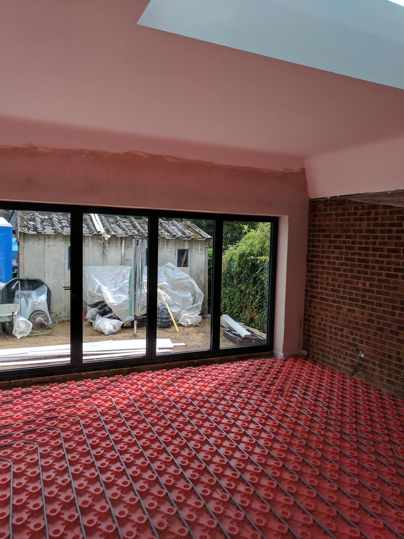 Newly plastered extension with black bifold doors installed and underfloor heating pipework laid across the floor