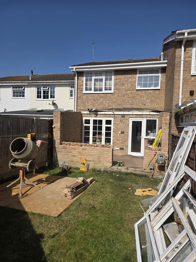 Rear extension under construction with new brickwork built up to sill height and the old windows stacked to one side