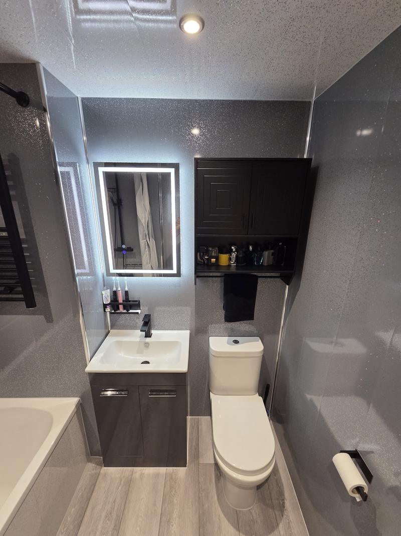 Refitted bathroom with a grey vanity unit, black tap, illuminated mirror and oak-effect floor