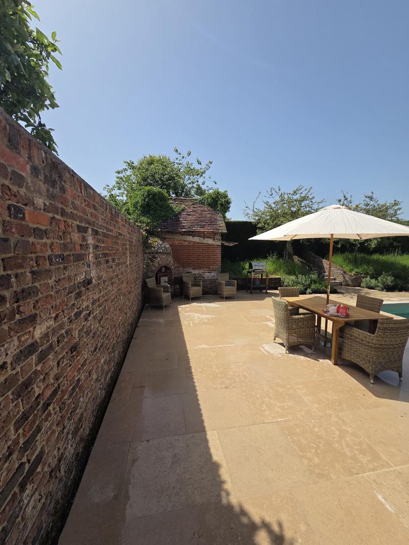 Sandstone terrace running alongside an old red brick garden wall with a table and chairs at the far end