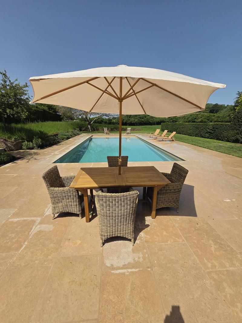 Sandstone terrace with a parasol, timber table and wicker chairs, the pool and open farmland beyond