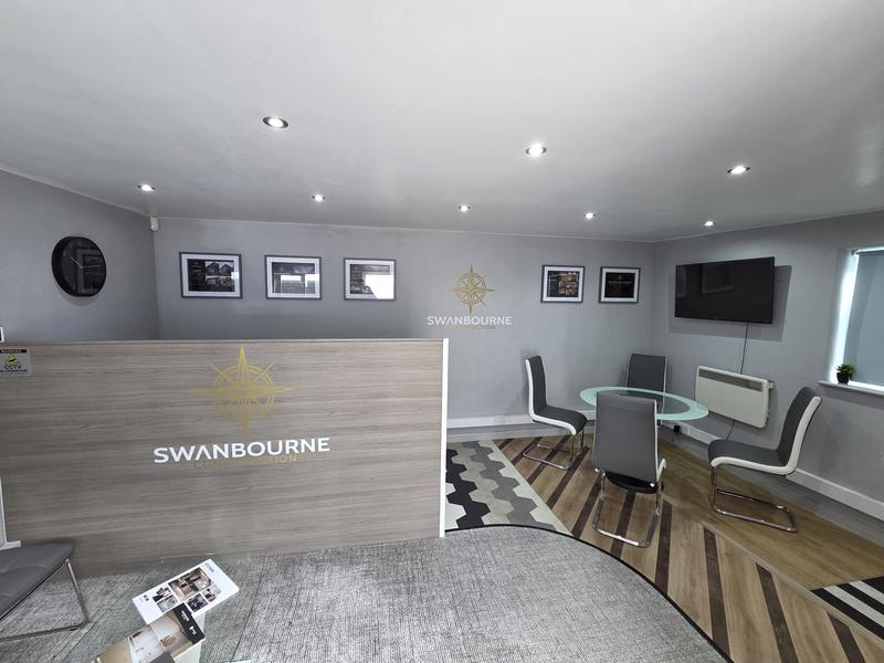 Showroom and office interior with a branded reception desk, framed panels on the wall and a meeting table beyond
