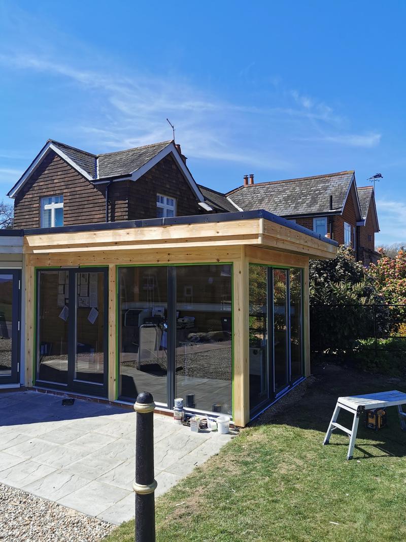 Single-storey rear extension with a flat roof, timber posts and full-height glazing onto a lawn