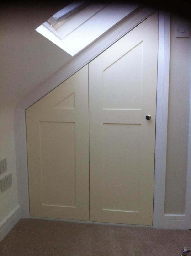 Storage doors built into the low eaves under a rooflight, each door cut to the angle of the roof slope