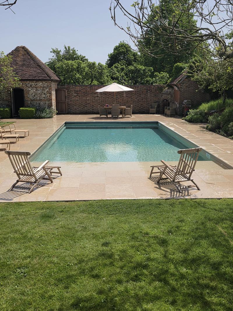 Swimming pool and sandstone terrace with the pool house beyond, seen across the lawn
