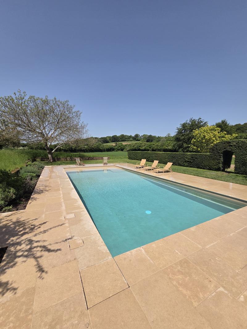 Swimming pool with the countryside beyond, sandstone paving running to the water's edge