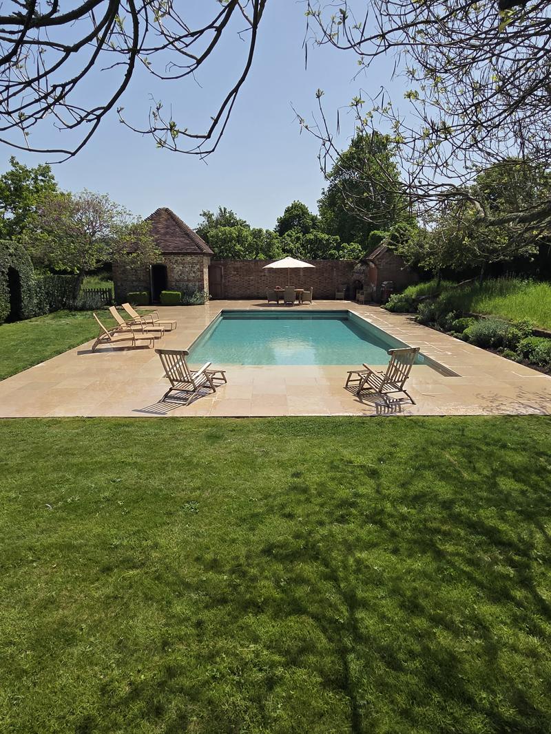 Swimming pool with turquoise water, cream sandstone terrace, timber loungers and a brick garden building beyond