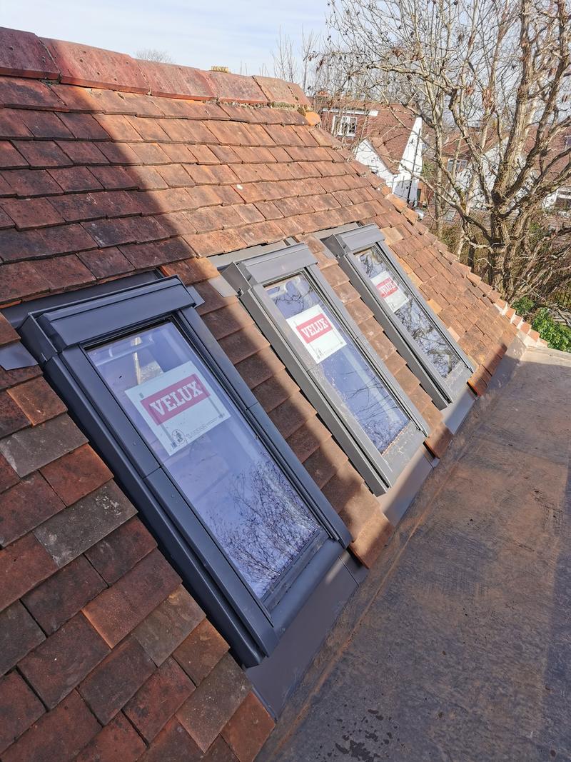 Three new grey roof windows installed into a clay plain-tile roof, protective labels still on the glass