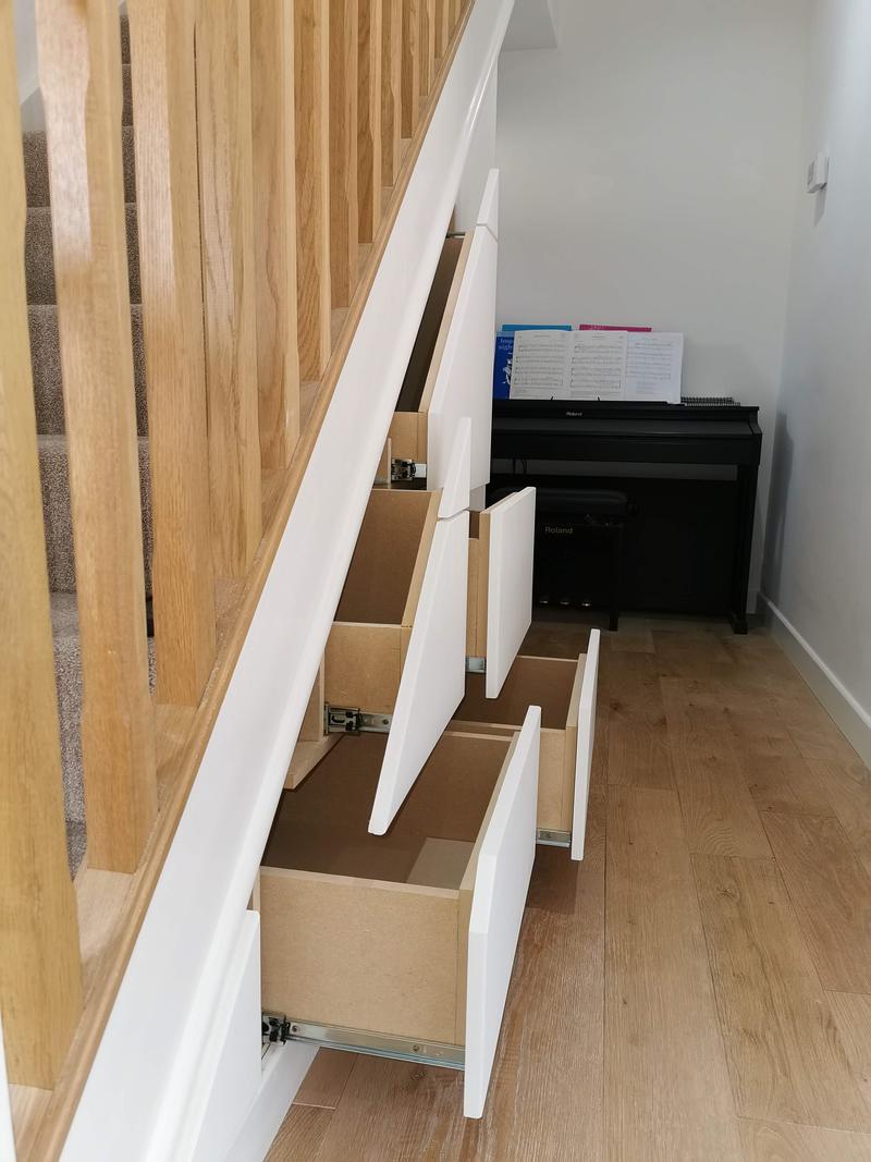 Under-stairs drawers pulled out to show bespoke storage beside an oak staircase