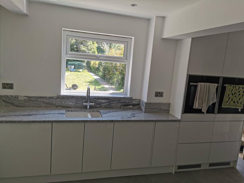 White gloss handleless kitchen with granite worktops and a garden view over the sink