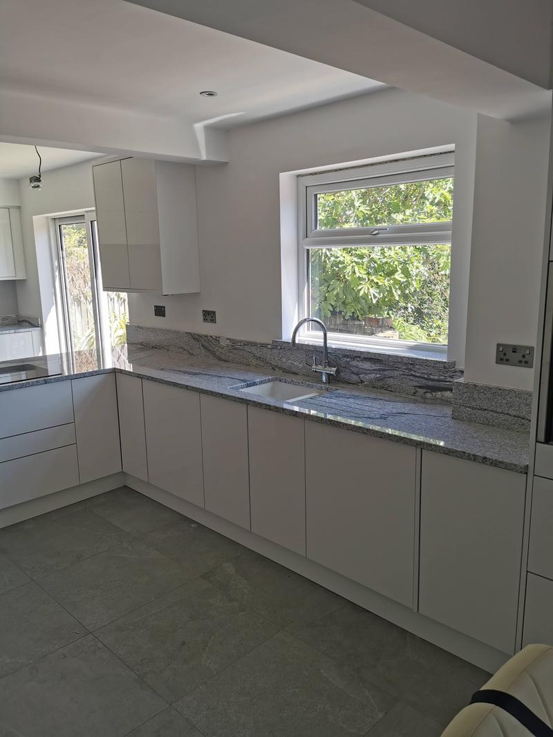 White gloss kitchen units beneath a speckled granite worktop and matching splashback